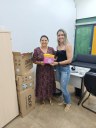 Para cego ver: Foto mostra duas mulheres ao centro da imagem segurando um pacote de absorventes